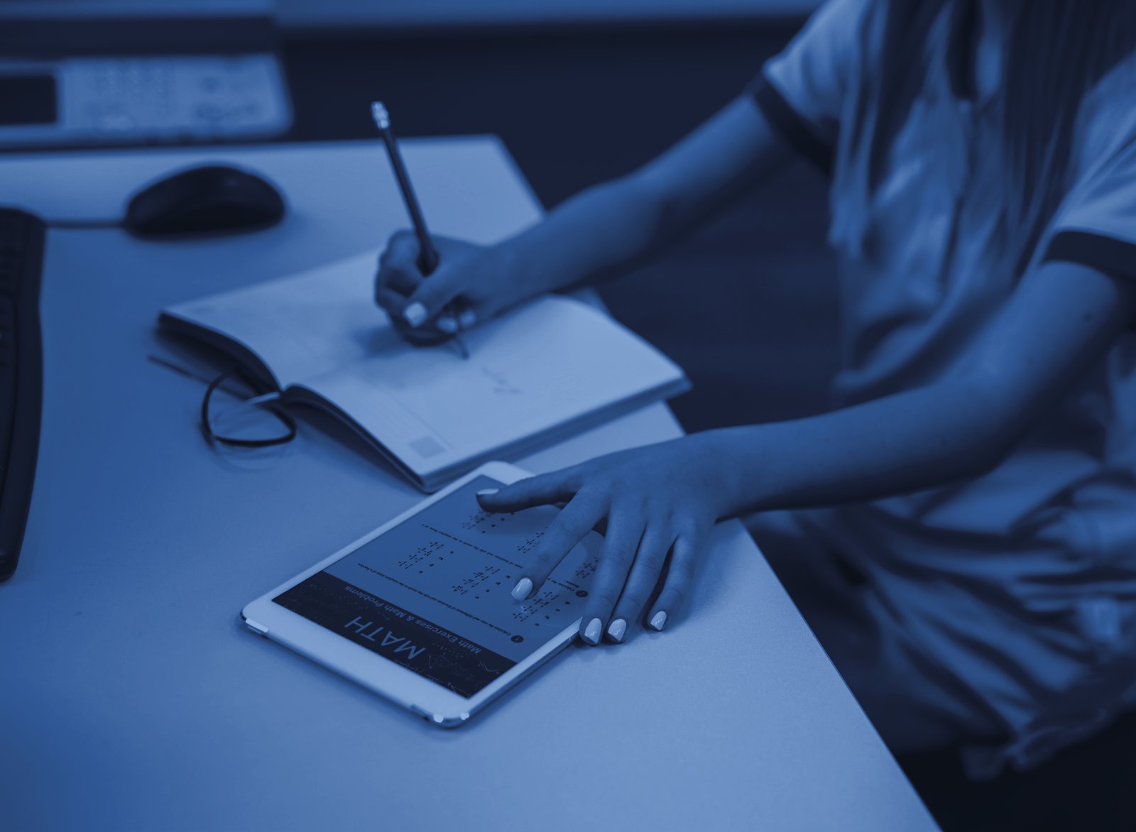 Studente che scrive su un quaderno accanto a un tablet